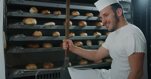 Slow motion of a handsome baker working at the bakery with breads and oven on the background.