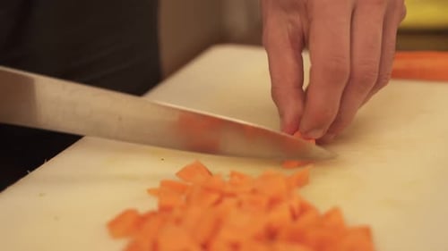 Close up view of a chef dicing carrot on cutting board. Trained hands chopping carrot precisely on a