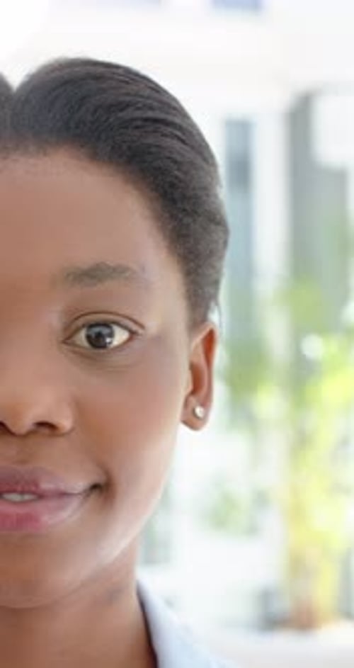 Vidéo verticale : Adolescente africaine regardant la caméra, souriant dans une pièce lumineuse avec un clou