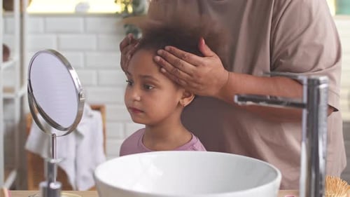 Adult Combs Child's Curly Hair in Bathroom