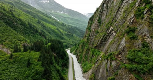 Drone footage along the steep cliff rock with a river at the foot. A highway goes along the river.