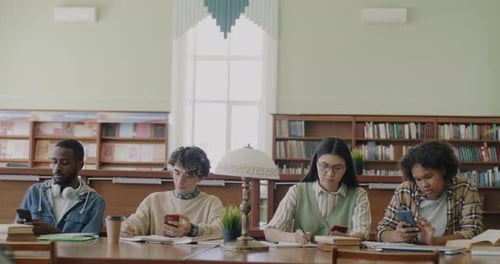 Multiethnic Group of Students Using Smartphones and Writing in Notebook Studying in University