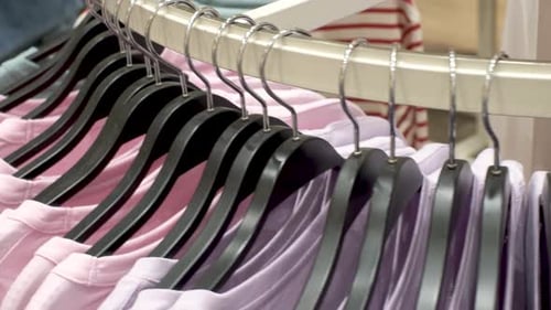 Multicolored cotton t-shirts hang on hangers in a store and rotate in circle close-up.