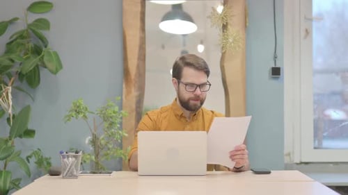 Man Works at Laptop Reading Documents at Desk