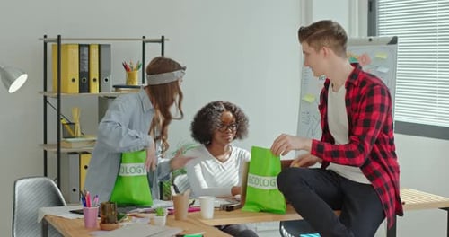 Colegas multirraciales con bolsas ecológicas hablando y usando una computadora portátil
