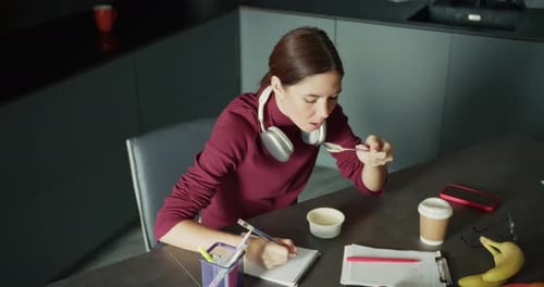 Young Adult Woman Writes While Eating at Table