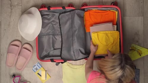 A Woman Packing a Peachcolored Suitcase with Summer Clothing and Travel Essentials of Top View