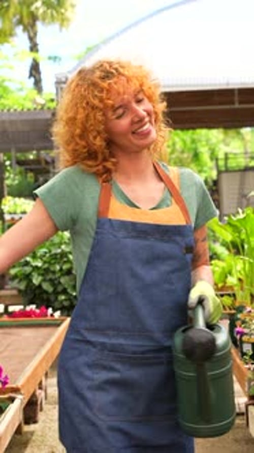 Gardener woman holding watering can smiling in greenhouse