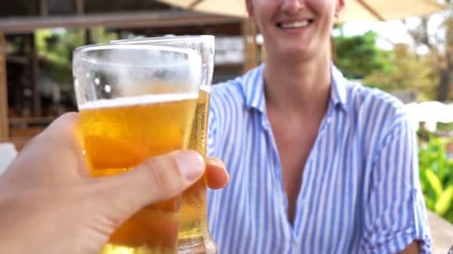 Happy couple cheers cold beers in garden cafe toasting to love and togetherness