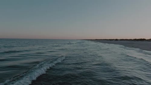 Low altitude drone shot, flying forward, over the mesmerizing waves hitting the white sand beach
