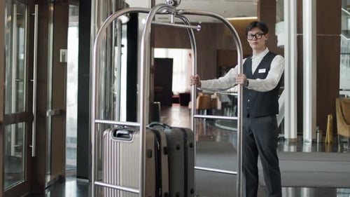 Bellhop With Luggage Trolley In Hotel Lobby