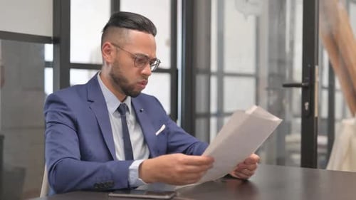 Young Adult Looks at Paperwork in Office Confused