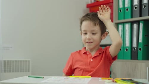 Boy Doing Schoolwork at Desk Raises Hand