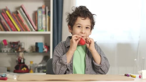 Child Inflates a Red Balloon at Table Indoors