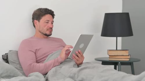 Man Using Tablet While Lying in Bed