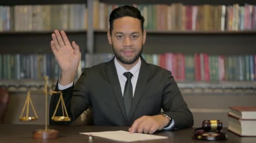 Abogado de mediana edad saludando con la mano para un chat de vídeo en la sala del tribunal