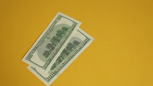 Hand picking up three hundred dollar bills on yellow background