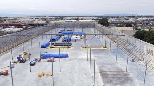 Roof of new warehouse under construction with building equipment and machinery, aerial view