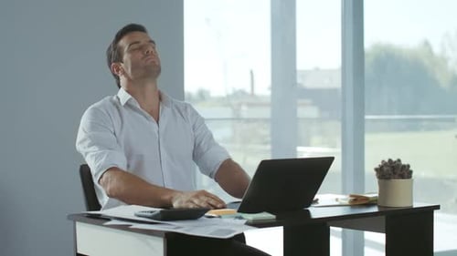 Man Stretches Neck At Desk While Using Laptop
