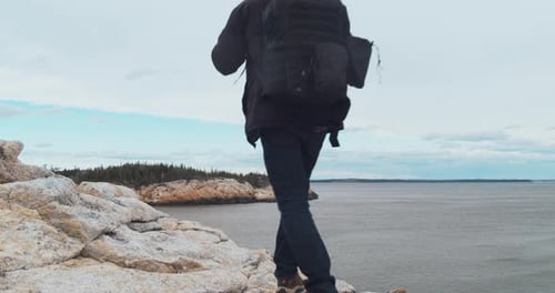 Man Standing with a Backpack on a Rocky Mountain and Looking at the Ocean