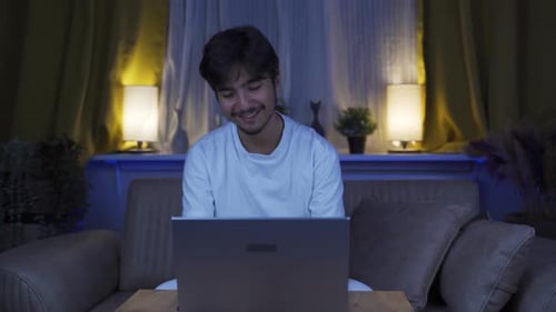 Laughing man using laptop at night.