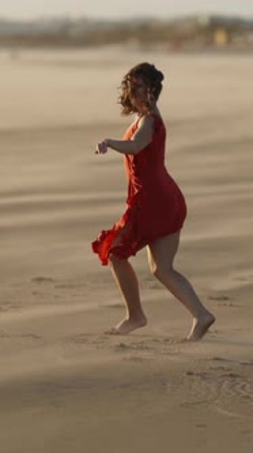 Graceful Young Woman in Red Dress Dancing on Sandy Beach