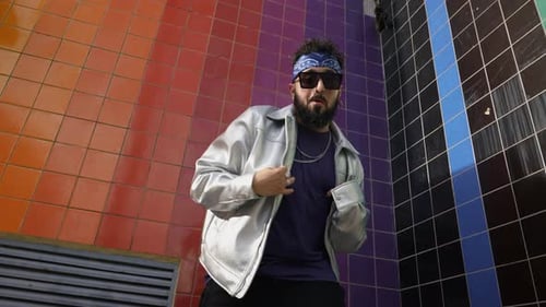 Stylish Man in Urban Fashion Dancing Against Tile Wall