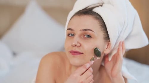 beautiful young girl doing a facial massage with a jade roller massager