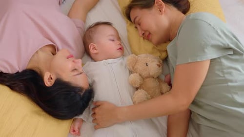 Asian lesbian couple lovingly caring for and raising their baby boy at home.