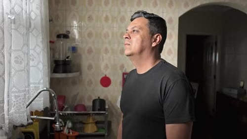 Man Standing in Kitchen Looking out Window Thoughtfully