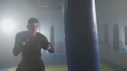 Aggressive Fighter Trains His Kicks and Punches in the Boxing Gym a Man Boxer Beats a Punching Bag