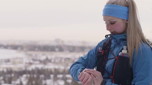 Female runner checking smartwatch on cold winter trail in Canada