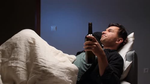 Man Lying Down Drinks from Bottle in Bedroom