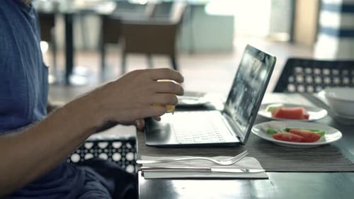 Man Using Laptop and Drinking Orange Juice by Table in Cafe 30s