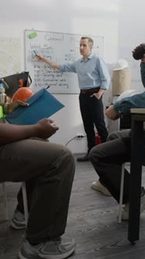 El equipo de construcción escucha al supervisor hablar en la pizarra blanca de la oficina