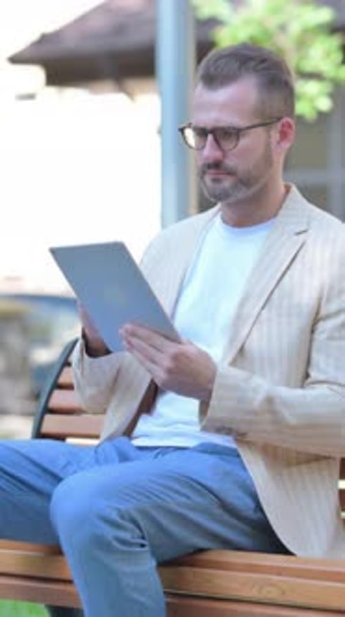 Man with Tablet Sitting and Talking on Bench