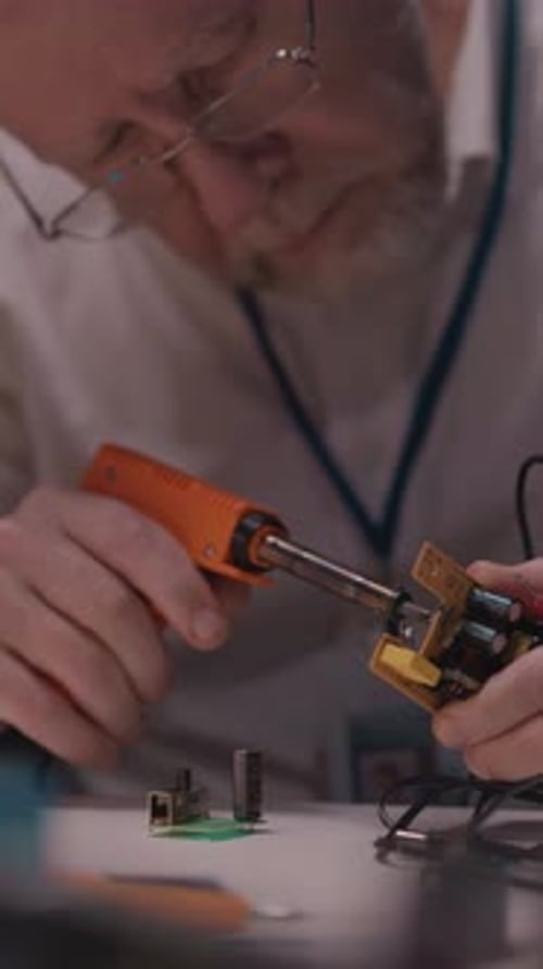 Adult Engineer Working Late in Office Repairing Microship Motherboard with Aoldering Iron Modern