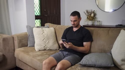 Young Man Using Phone on Couch at Home