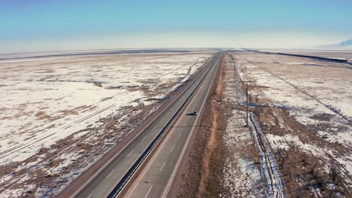 Silver van drives through snow covered steppe - aerial view, drone flight