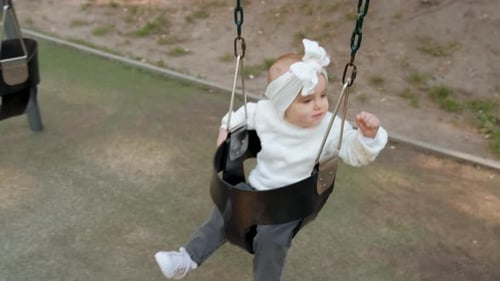 Baby Girl with Bow on Her Head is Swinging on a Swing in the Park Little Child on the Playground