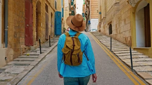 A Female Tourist in a Hat and with a Backpack Walks Along the Traditional Old Streets and Looks at