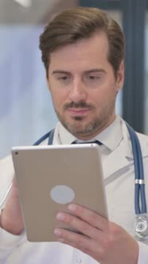 Concentrated Man in Doctor's Coat Using Digital Tablet