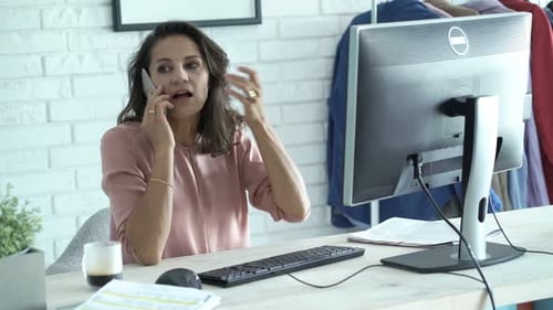 Young Businesswoman Talking on Cellphone Sitting by Desk in Office Adult