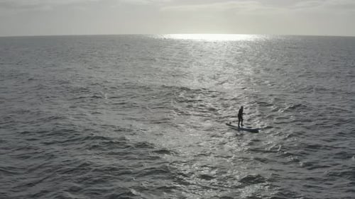 Man on stand up paddleboard silhouetted in sun beam and ocean swell