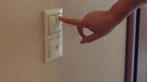 Pressionando manualmente o interruptor de luz na parede bege, ligando a eletricidade em ambientes fechados