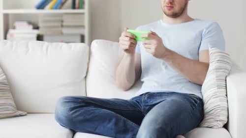 Young Adult Playing Video Game on Smartphone At Home