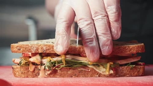 Hand Cuts Delicious Sandwich in Half on Board
