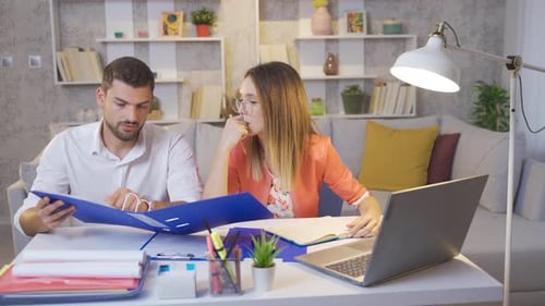 Married couple working at home in the evening looking at files and laptop.