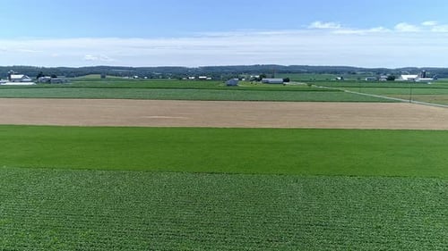 The landscape showcases expansive green fields interspersed with golden patches. Rolling hills and a