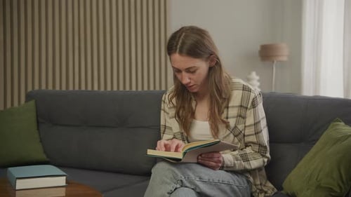 Young Woman Reads Book on Couch at Home